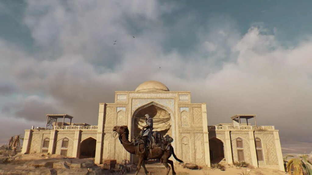 Jak zdobyć skrzynię z wyposażeniem opuszczonego karawanseraju w Assassin’s Creed Mirage Image showcasing the Abandoned Caravanserai in Assassin's Creed Mirage. Basim is on a camel and there are birds in the skies also.
